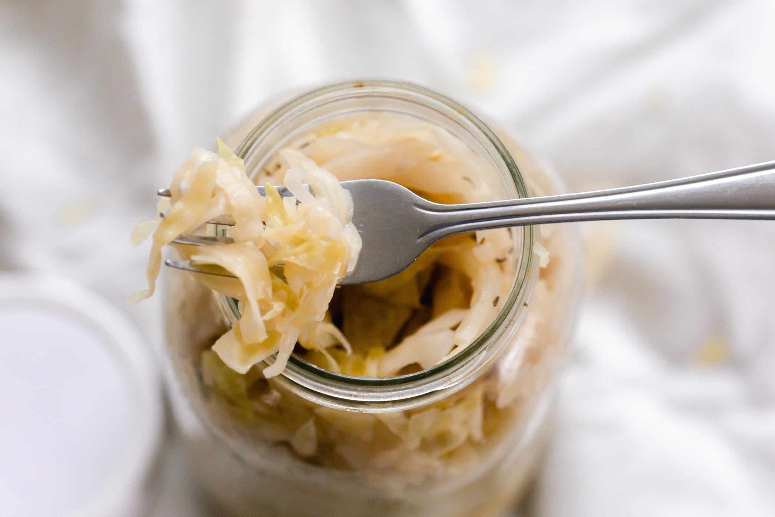 A fork scooping sauerkraut out of a mason jar.