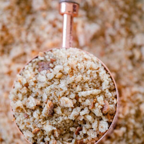 a copper and wood dry measuring cup full of sourdough bread crumbs on a sheet of more breadcrumbs