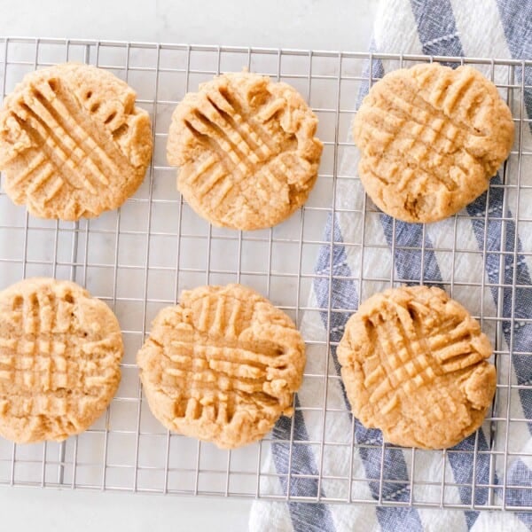 six sourdough peanut butter cookies on a wire rack on a white countertop with a blue and white tea towel