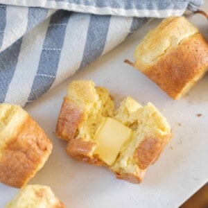 sourdough popover with butter on a white countertop next to a blue and white striped tea towel