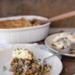 Shepherds pie on a white plate with a baking dish in the background.