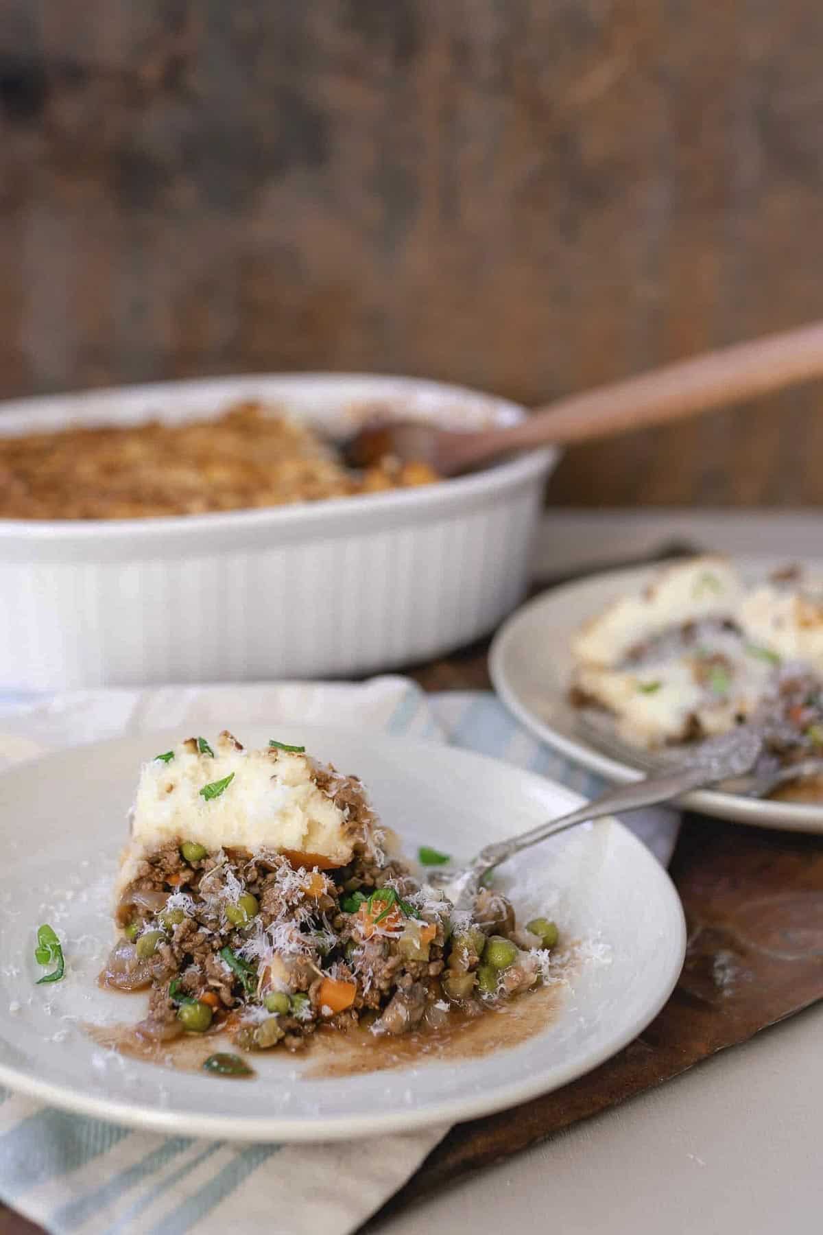 Shepherds pie on a white plate with a baking dish in the background.