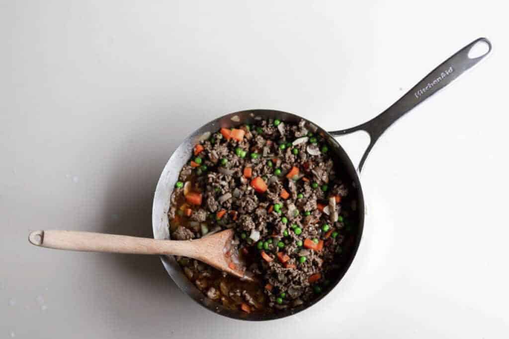 shepherd pie filling in a saucepan with a wooden spoon.