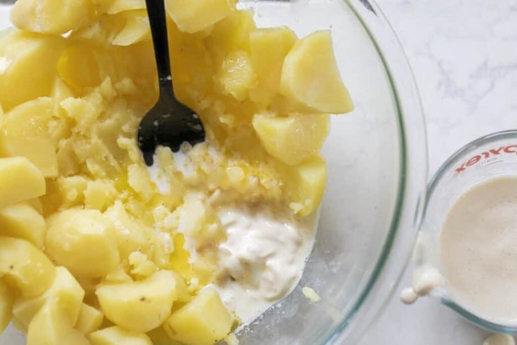 potatoes being mashed with butter and cream in a glass bowl.