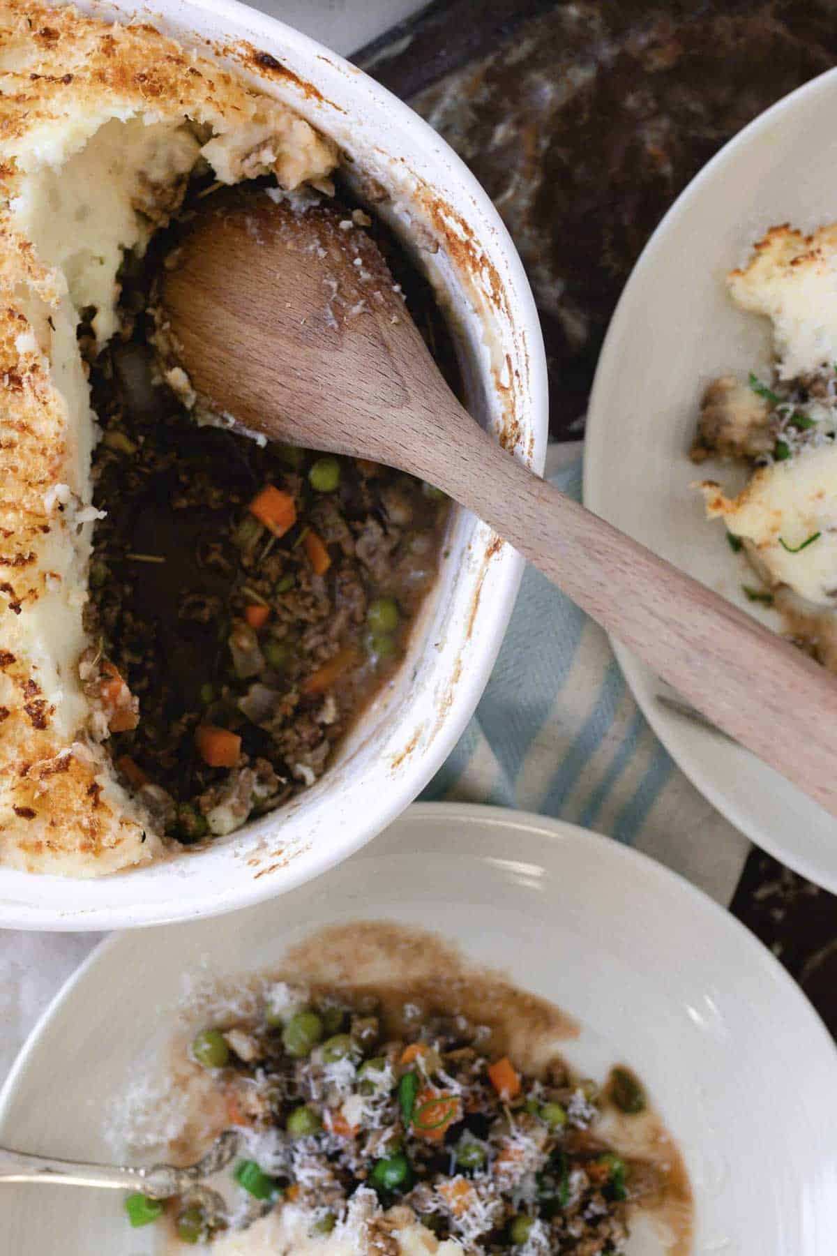 two plates and a baking dish of Shepards pie. Ground beef and veggies topped with mashed potatoes.