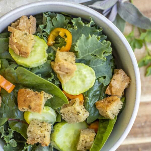 overhead photo of a kale salad topped with cucumbers, sliced peppers, and gluten free croutons