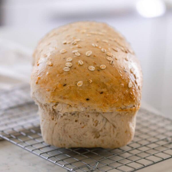 loaf of sourdough multigrain bread on a wire rack on a white countertop with a white towel in the background