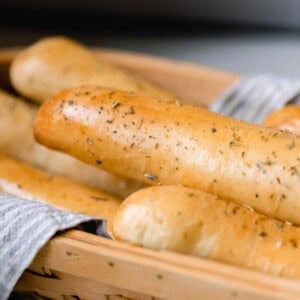 a towel lined basket full of sourdough bread sticks topped with a herb garlic butter