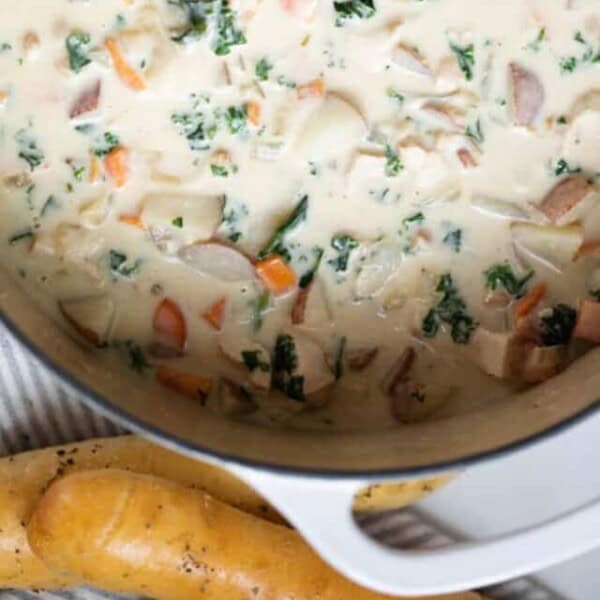 A pot of chicken kale soup on the counter with a dish of breadsticks sitting nearby