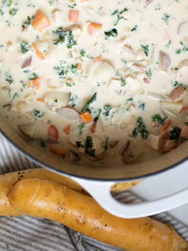 A pot of chicken kale soup on the counter with a dish of breadsticks sitting nearby