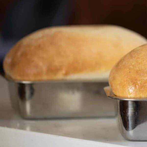 Two golden brown loaves of sourdough bread using a potato flake sourdough starter. Both loaves are in tin loaf pans on a white counter top