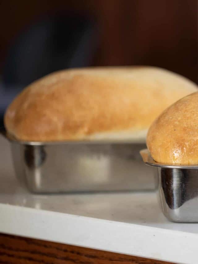 Two golden brown loaves of sourdough bread using a potato flake sourdough starter. Both loaves are in tin loaf pans on a white counter top