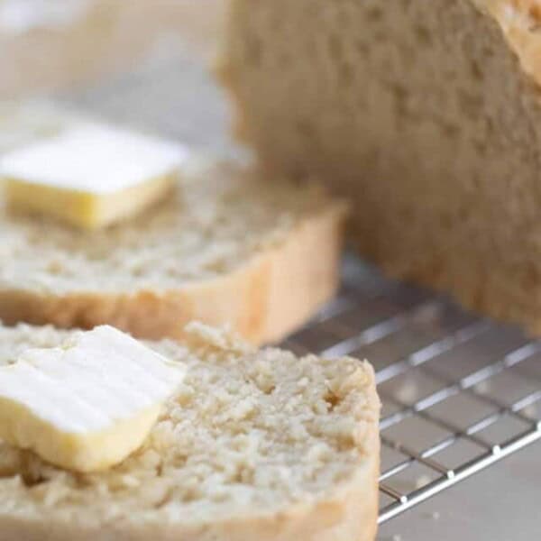 A loaf of sourdough beer bread cut with two slices with a tab of butter on each sitting on a wire rack