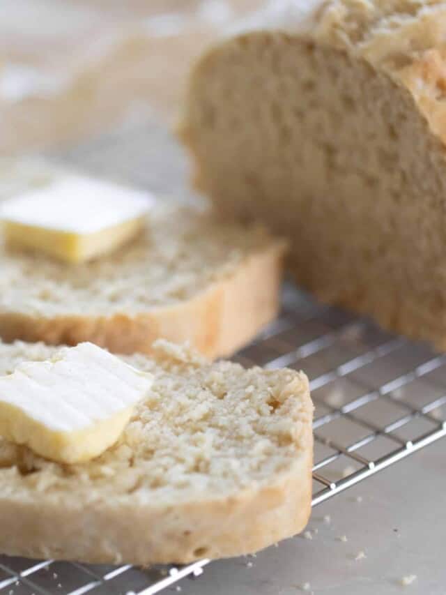 A loaf of sourdough beer bread cut with two slices with a tab of butter on each sitting on a wire rack