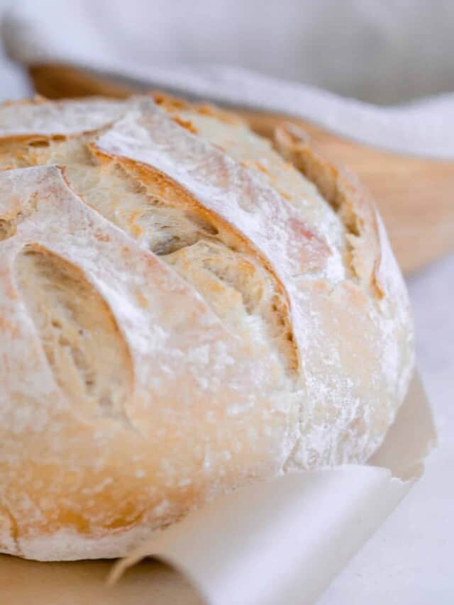 sourdough bread with a leaf pattern on parchment paper with a copper container to the left