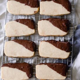 eight sourdough shortbread cookies with the corners dipped in chocolate sitting on a cooling rack on the counter