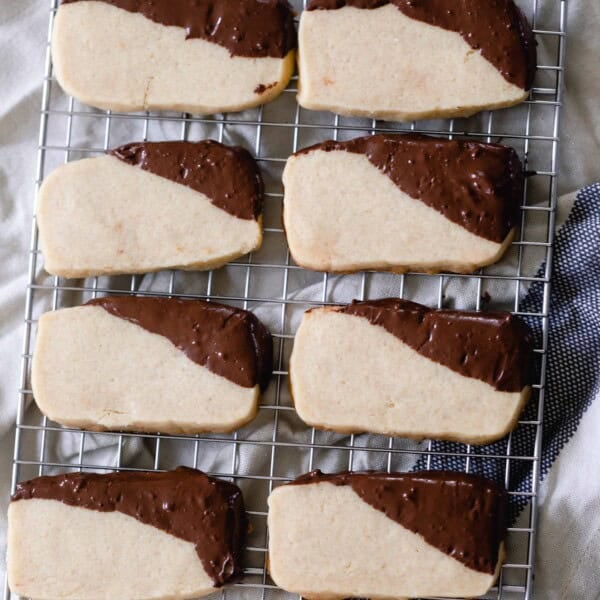 eight sourdough shortbread cookies with the corners dipped in chocolate sitting on a cooling rack on the counter