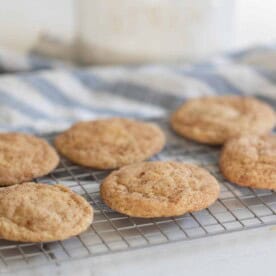 six sourdough snickerdoodle cookies on a wire cooling rack over a blue and white stripped towel