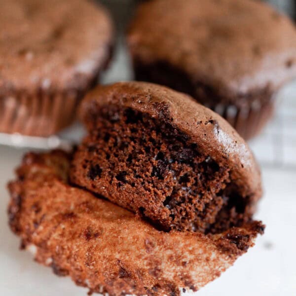 An einkorn protein muffin with the liner off to show texture and other muffins in background on cooling rack on a white counter top