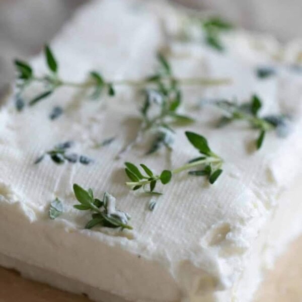 A square block of Greek yogurt cream cheese with herbs on top on a piece of parchment paper