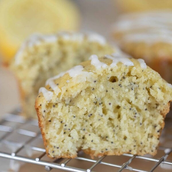 sourdough lemon poppyseed muffin sliced in half of a wire rack. Another muffin and a half of a lemon are in the background