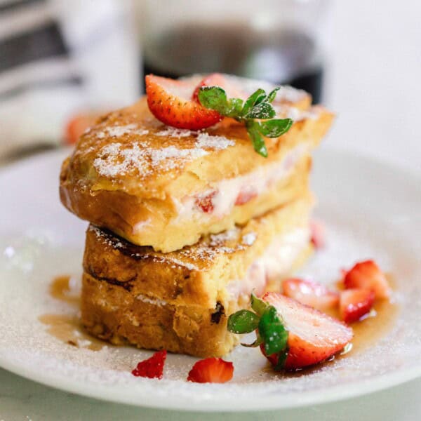 Strawberry stuffed French toast sliced in half and stacked on top of each other topped with powdered sugar and fresh strawberries on a white plate