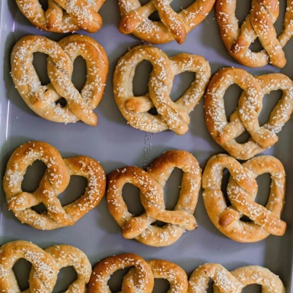 Baking sheet with freshly baking homemade sourdough pretzels topped with coarse salt