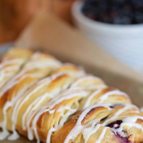 sourdough pastry braid with blueberry cream cheese filling drizzled with icing on parchment paper with a bowl of blueberries in the background