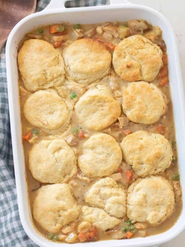 overhead photo of chicken pot pie topped with sourdough biscuits in a white baking dish on a white and blue checked towel