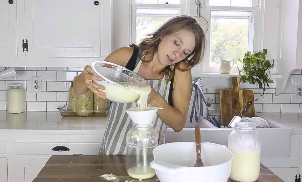 Woman pouring strained milk kefir into a jar.