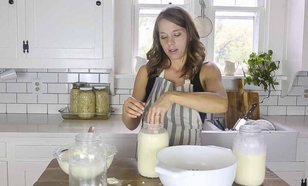 woman adding kefir grains to a mason jar of milk.