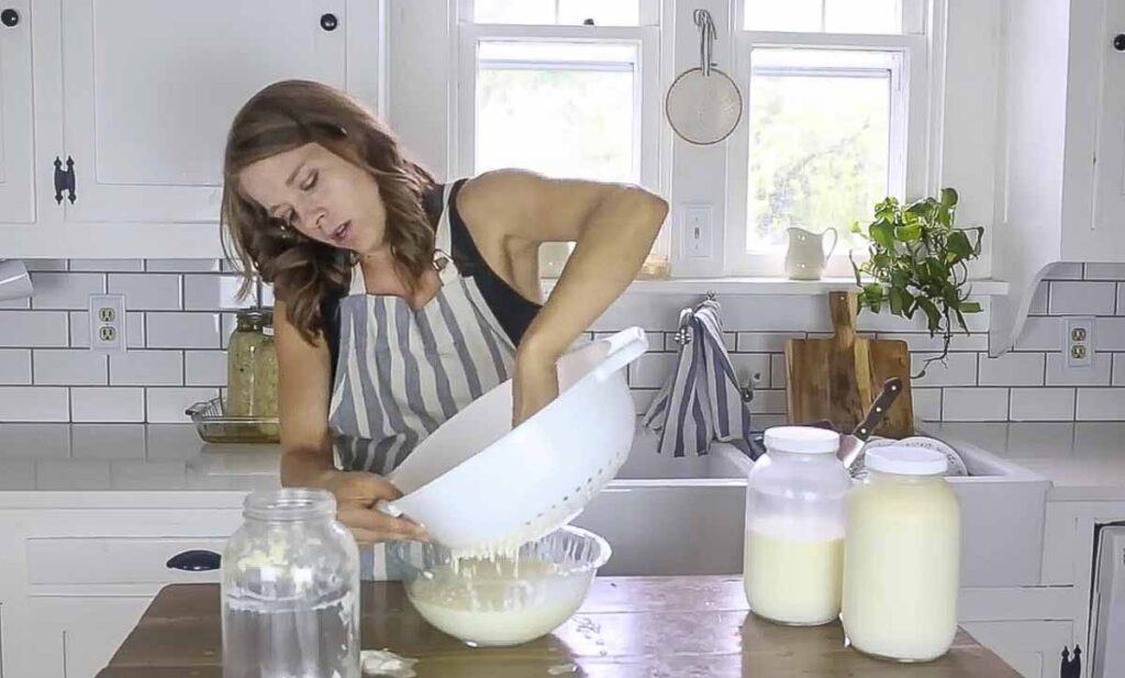 A woman strainer milk kefir into a bowl.