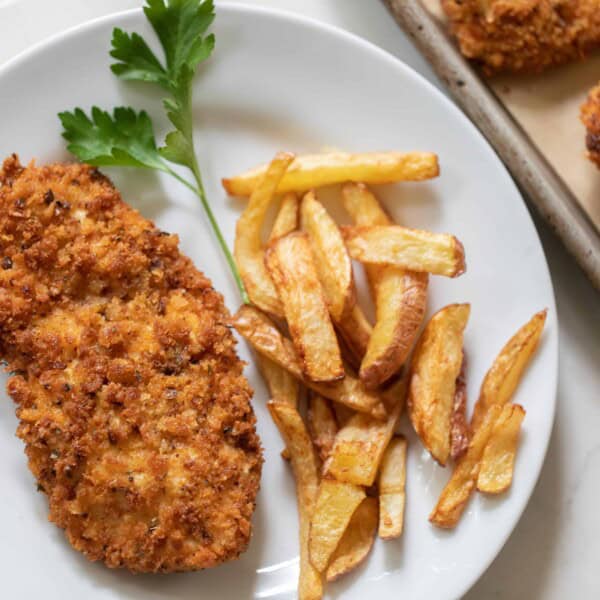 overhead photo of sourdough fried chicken with French fries and a sprig of parsley on a white plate