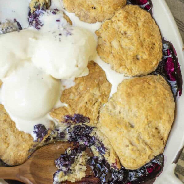 overhead photo of sourdough blueberry cobbler topped with ice cream with a wooden spoon in the cobbler