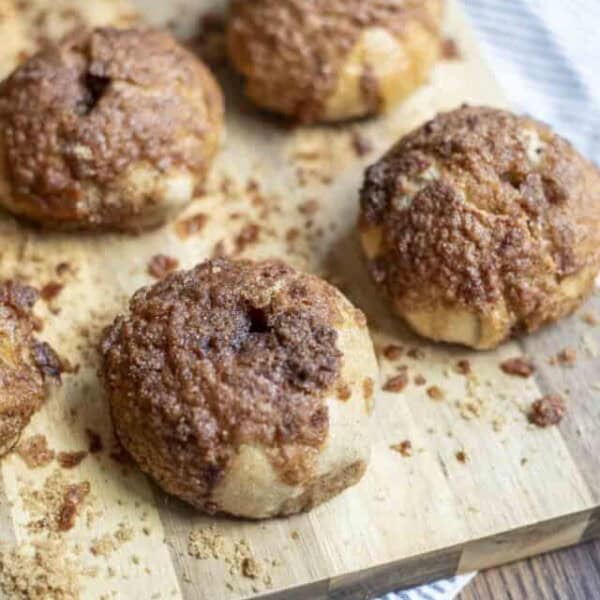 5 sourdough cinnamon crunch bagels on a wood cutting board on a white and blue stripped towel