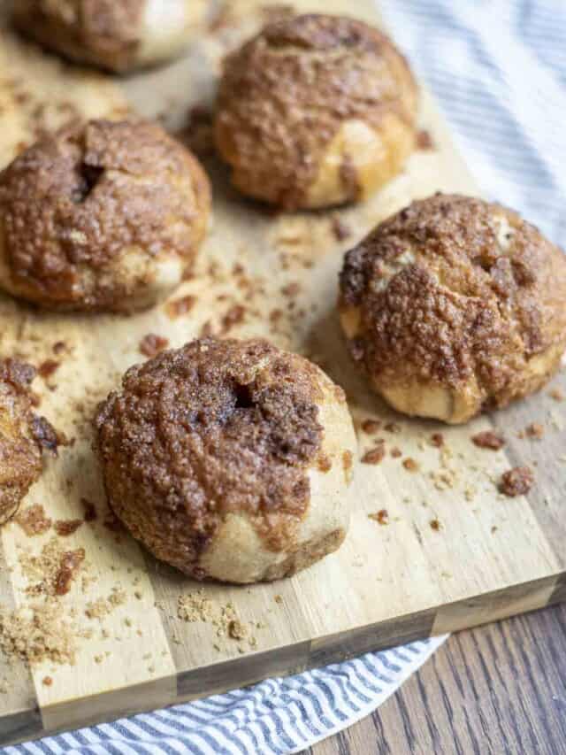 5 sourdough cinnamon crunch bagels on a wood cutting board on a white and blue stripped towel