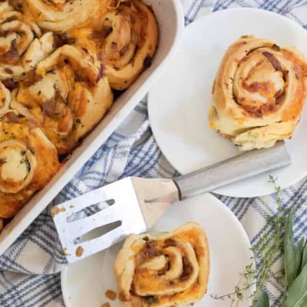 overhead photo of sourdough herb and cheese rolls in a baking dish with two plate with rolls to the right on a top of a blue and white plaid towel