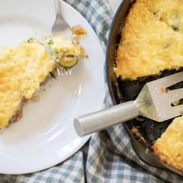 sourdough skillet topped with cheese and parsley in a cast iron skillet with a slice cut out. The slice is on a white plate on a blue checked towel