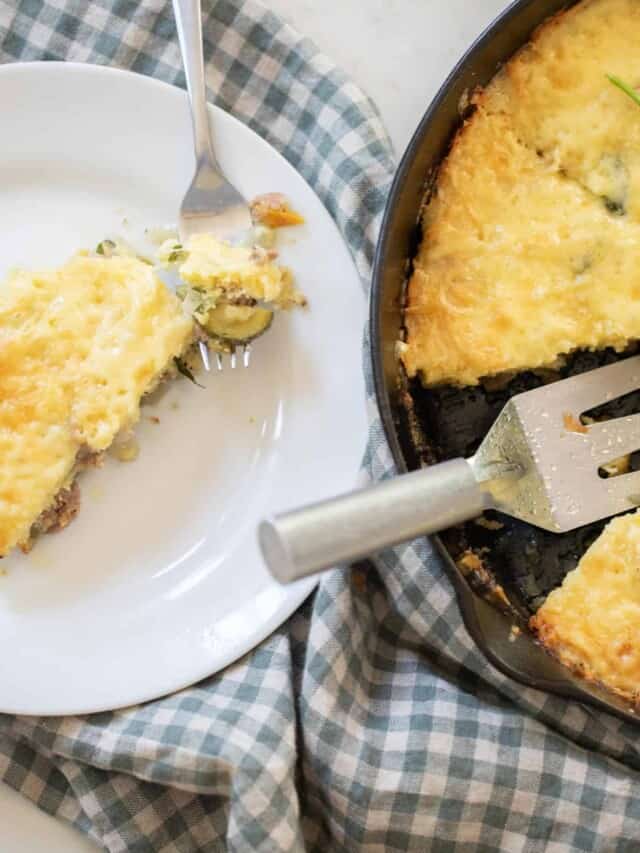 sourdough skillet topped with cheese and parsley in a cast iron skillet with a slice cut out. The slice is on a white plate on a blue checked towel