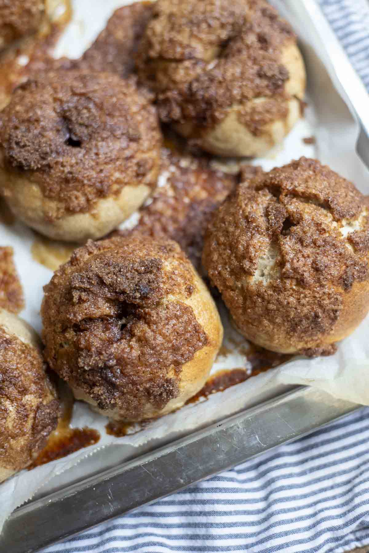 four sourdough cinnamon crunch bagels on a parchment lined backing sheet on a blue stripped towel.