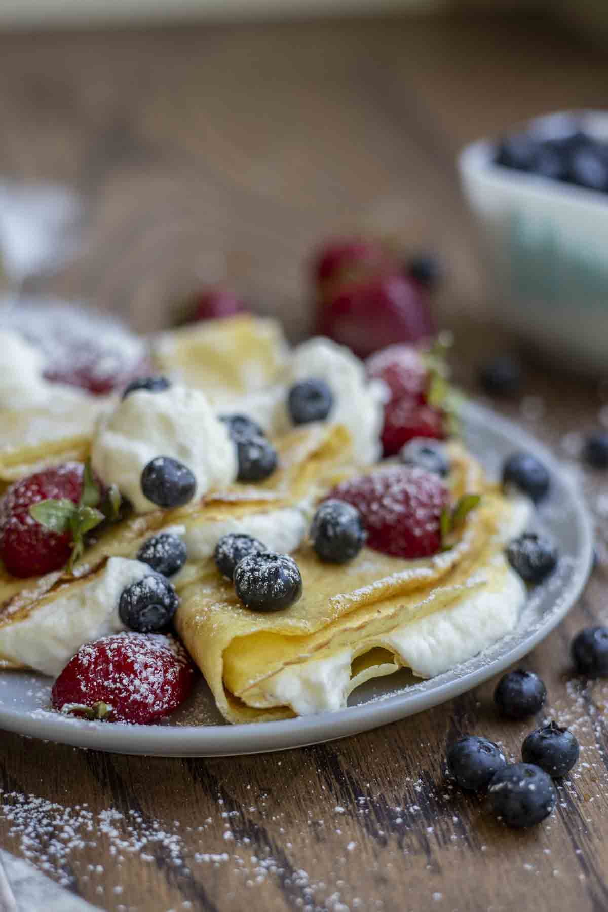 Plate of folded sourdough crepes with whipped cream, strawberries, and blueberries.