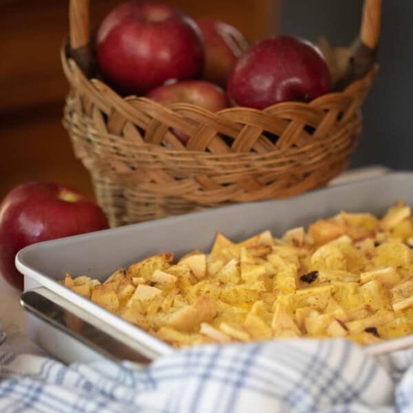 sourdough French toast casserole with raisins and apples in a baking dish with a basket of apples in the background