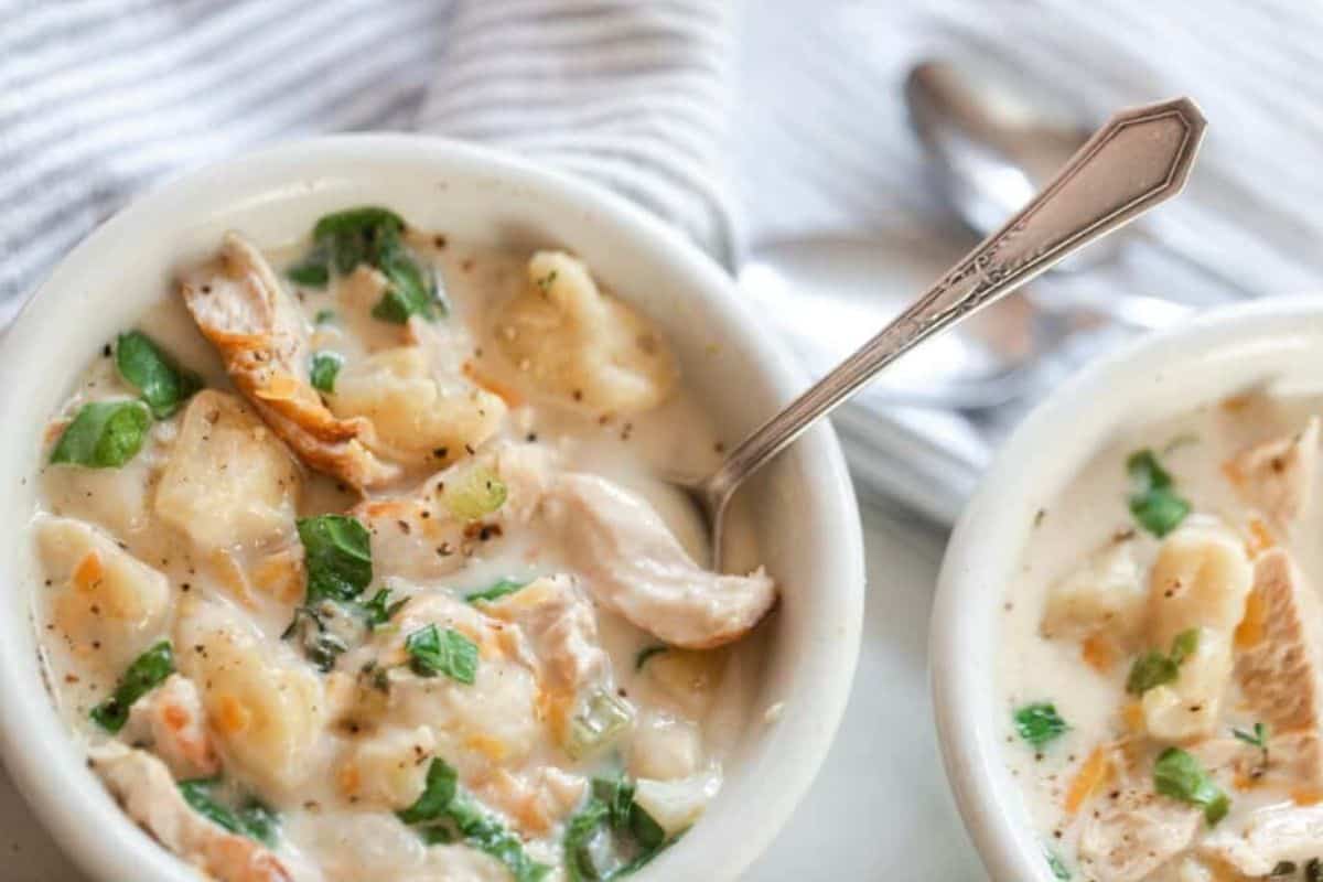 A bowl of creamy chicken soup with gnocchi with a silver spoon sticking out.