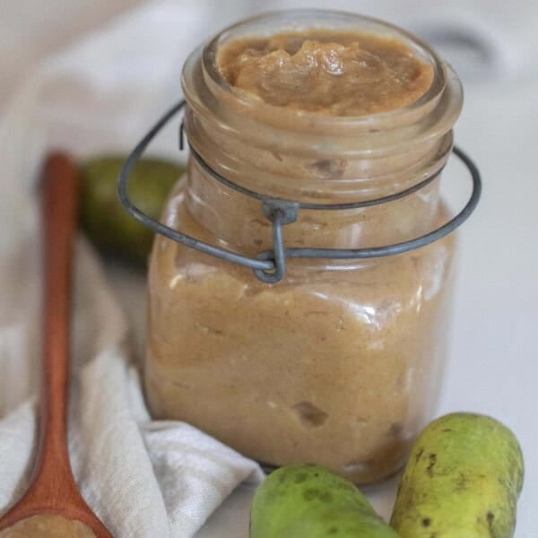 a swing top mason jar with pawpaw jam on a white towel with fresh pawpaw and a wooden spoons with jam in front of the jar