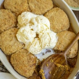 overhead photo of sourdough pumpkin cobbler topped with vanilla ice cream in a baking dish. A teal bowl with brown sugar is in the background