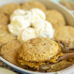 a wooden spoon taking out sourdough pumpkin cobbler topped with ice cream from a baking dish