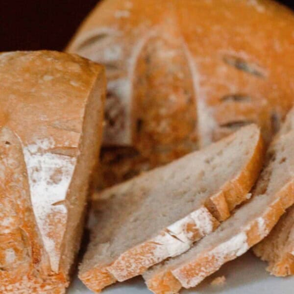 A sourdough boule cut into two halves with one cut into slices on white countertop with knife in background