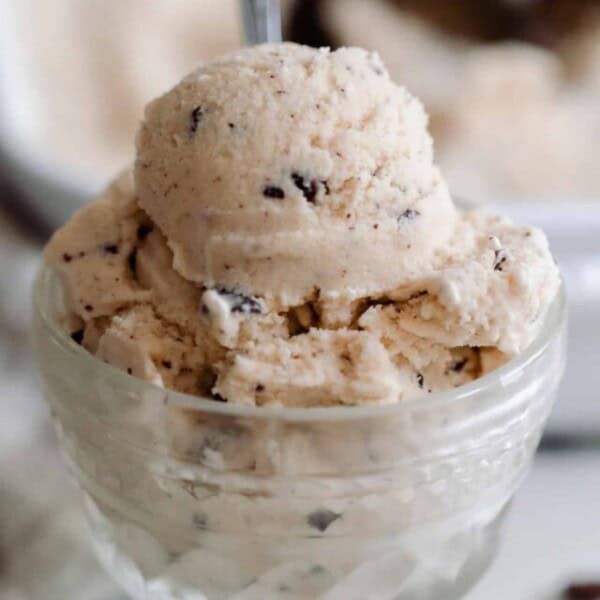 java chip ice cream in a vintage ice cream dish on a white countertop with chocolate chips, a towel and a baking dish of more ice cream in the background