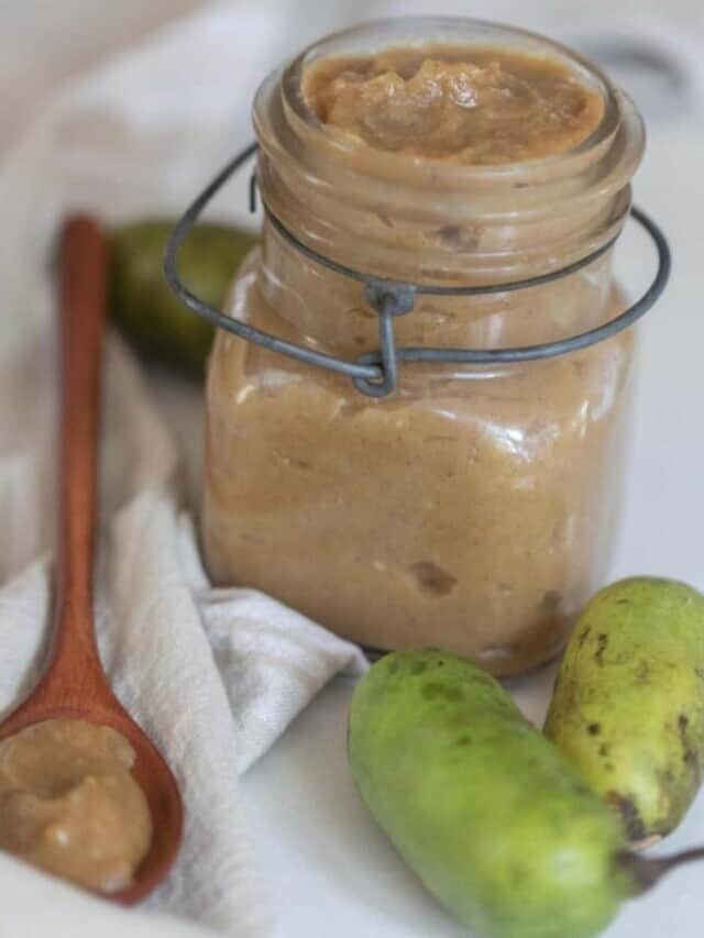 a swing top mason jar with pawpaw jam on a white towel with fresh pawpaw and a wooden spoons with jam in front of the jar