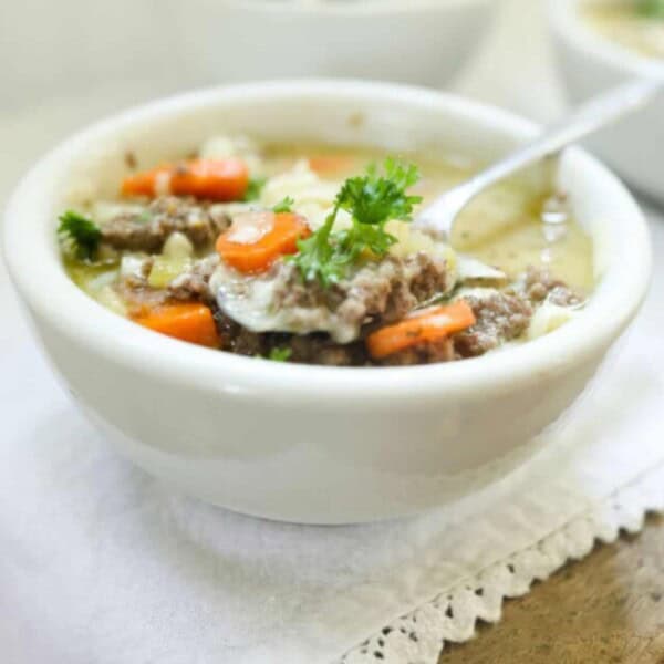 3 bowls of cheeseburger soup in white bowls with spoons on top of a wood table with white table runner.